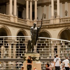 A classical statue in a historic courtyard with visitors in Milan, Italy.
