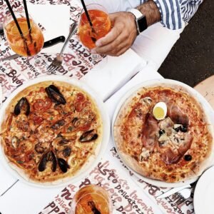 Top view of classic Italian pizzas with Aperol Spritz drinks on a table in Rome, Italy.